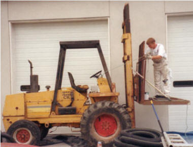 Worker uses long handle to operate controls of fork truck