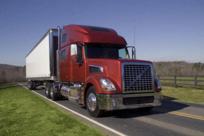 Bronze Volvo Truck with white "dry van" trailer out on a country road. 18 wheeler in the country